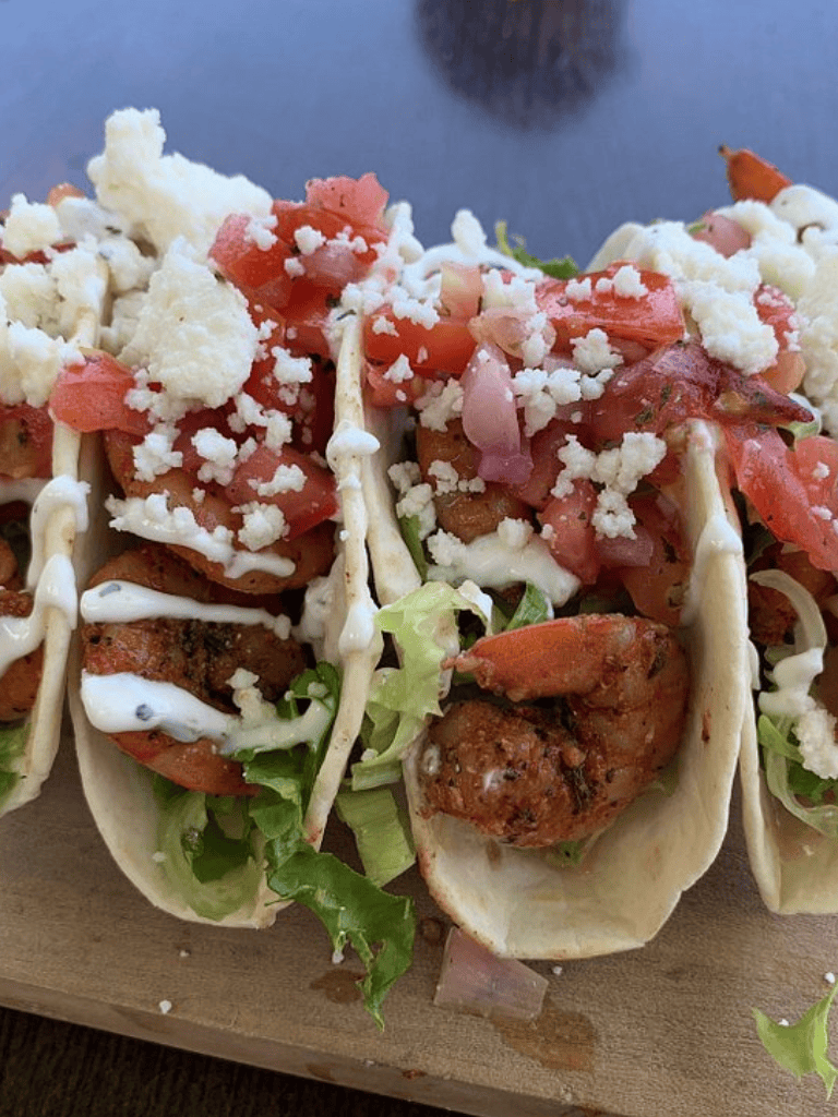Fresh lobster tacos with lettuce, tomato, cheese, and creamy sauce on a wooden board.