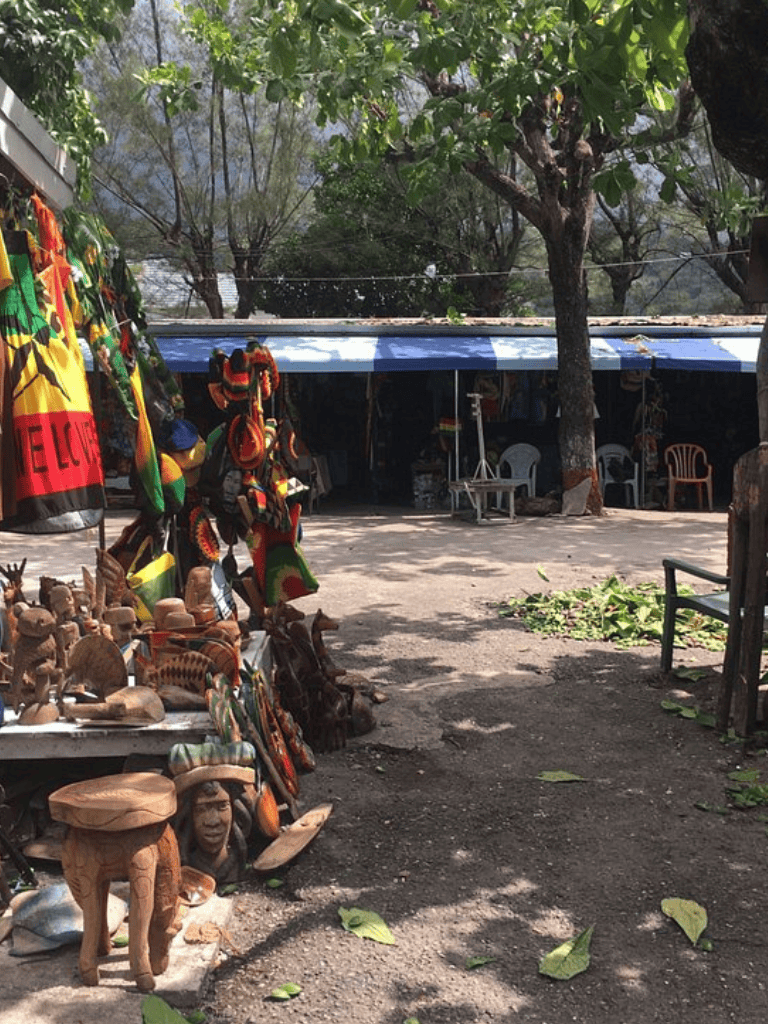 Colorful African crafts and souvenirs displayed at an outdoor market stall in a lush green setting.