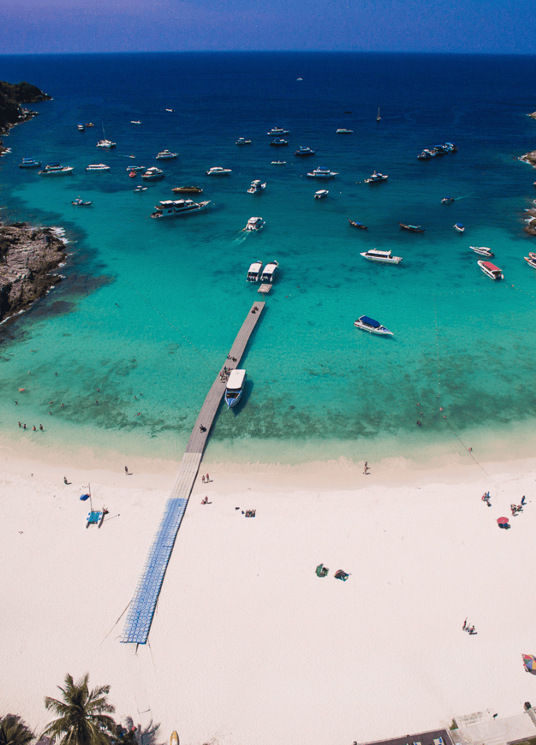 Boats anchored in turquoise ocean with sandy beach and pier at QuestForDirections coastal destination.