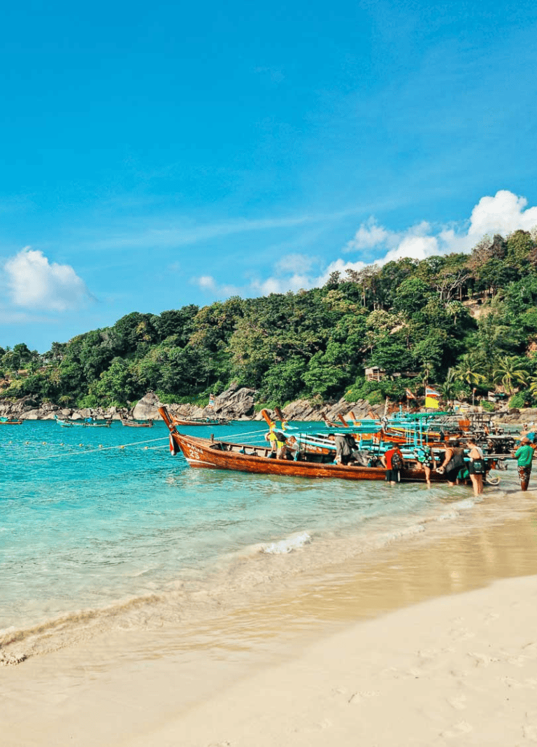 Colorful boats anchored at tropical beach with lush hillside in background.