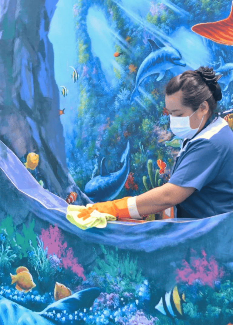 Colorful underwater-themed mural at Quest for Directions cleaning with a woman wearing a face mask and gloves.