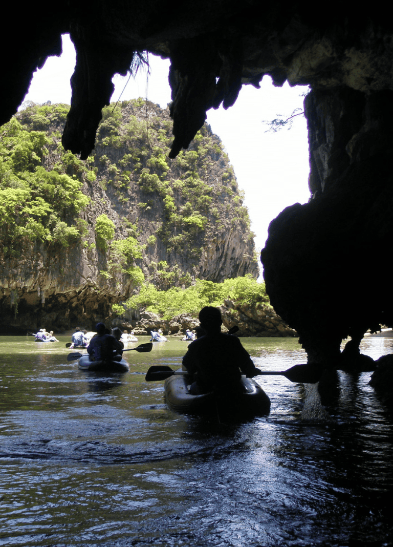 Kayaking through a scenic cave with lush green cliffs in the background.