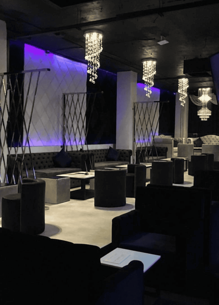 Elegant lounge in a modern nightclub with stylish chandeliers and ambient purple lighting.
