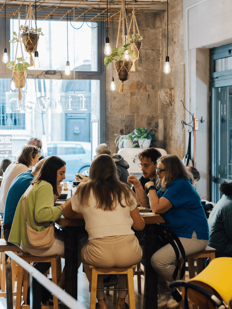 People dining at a cozy cafe with hanging plants and warm lighting inside.
