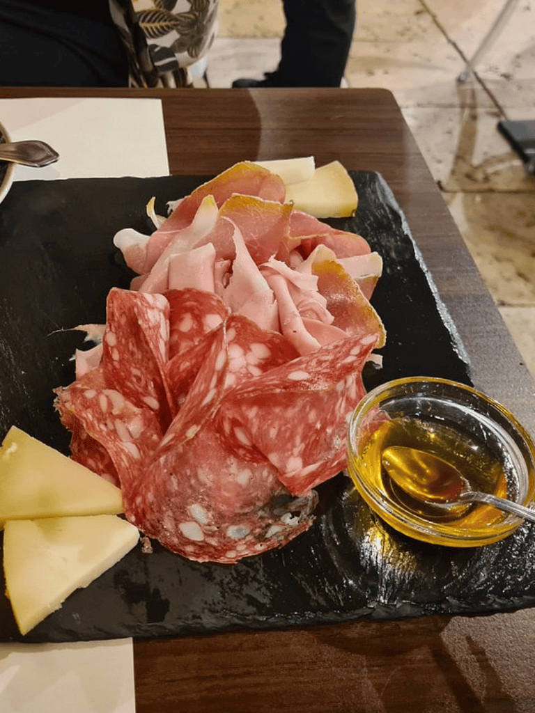 Assorted cured meats and cheese platter with honey for authentic Italian charcuterie experience.