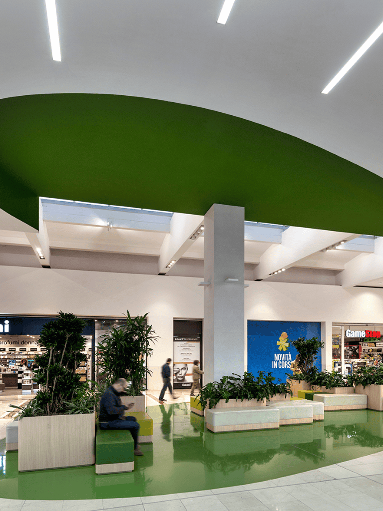 Bright modern shopping mall interior with seating and greenery, emphasis on retail stores and comfortable space.