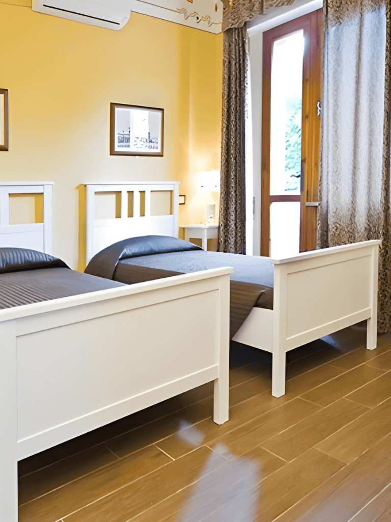 Comfy hotel room with twin beds, wooden flooring, bright yellow walls, and balcony access.