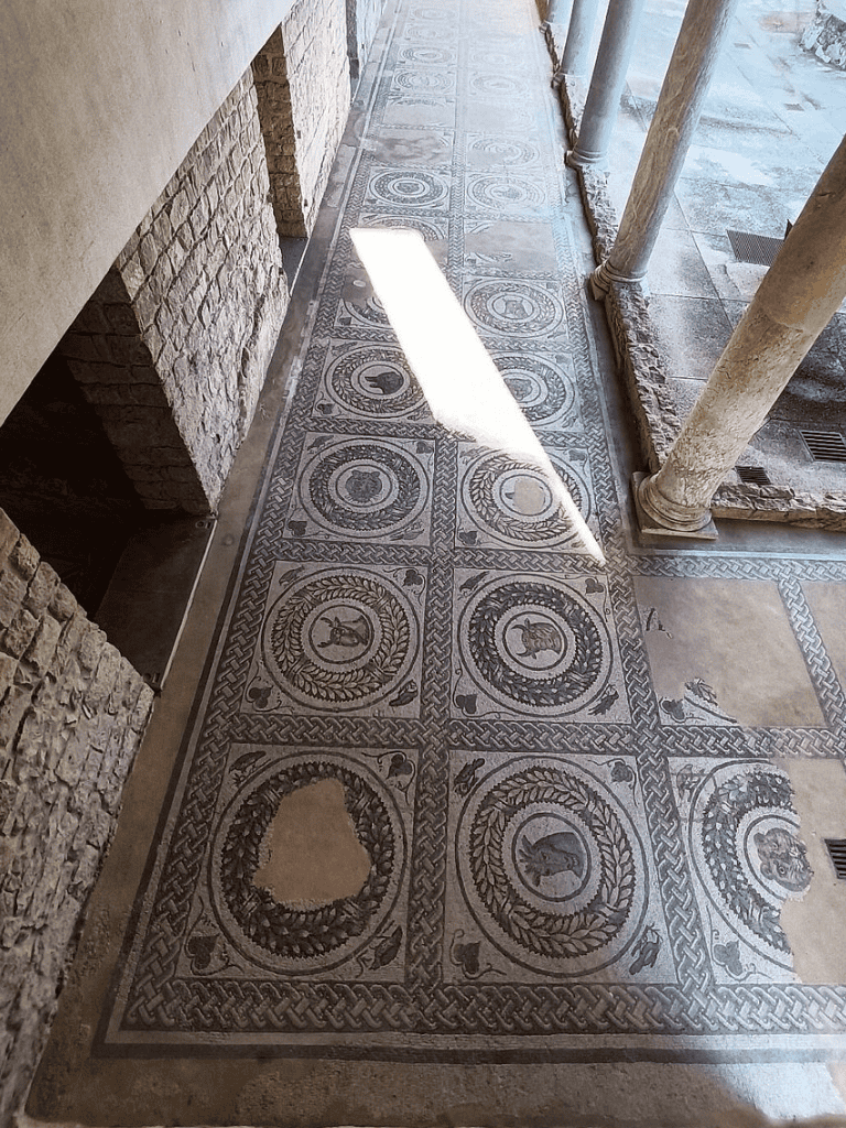 Ancient mosaic flooring with animal motifs and decorative borders in historical building reconstruction.
