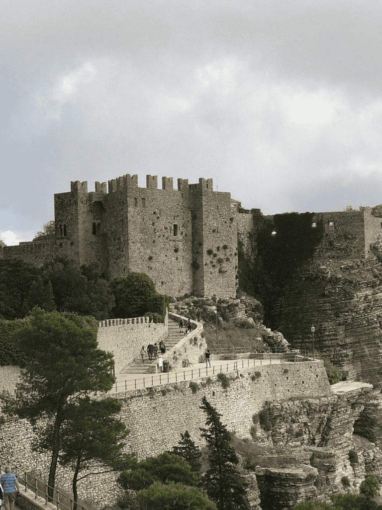 Medieval castle on rocky hillside with scenic viewing platform and lush greenery.