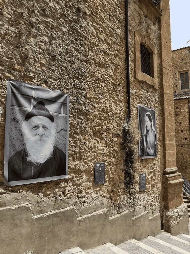 Black and white portraits display on a historic stone wall, highlighting local art and culture in an ancient European setting.