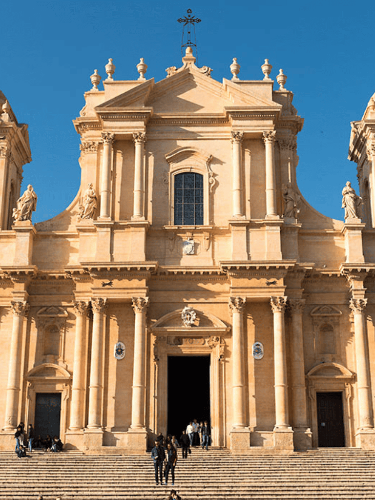 Ancient Baroque church with grand steps and detailed architectural facade against blue sky.