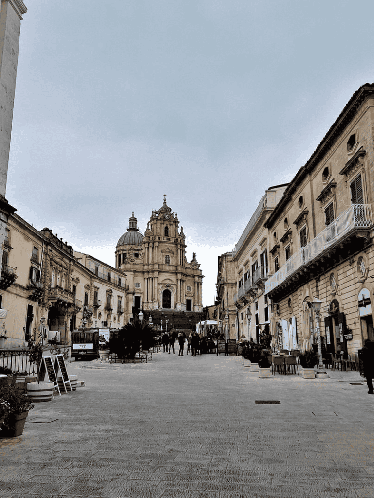 Ancient European city square with historic architecture and a grand church in the background.