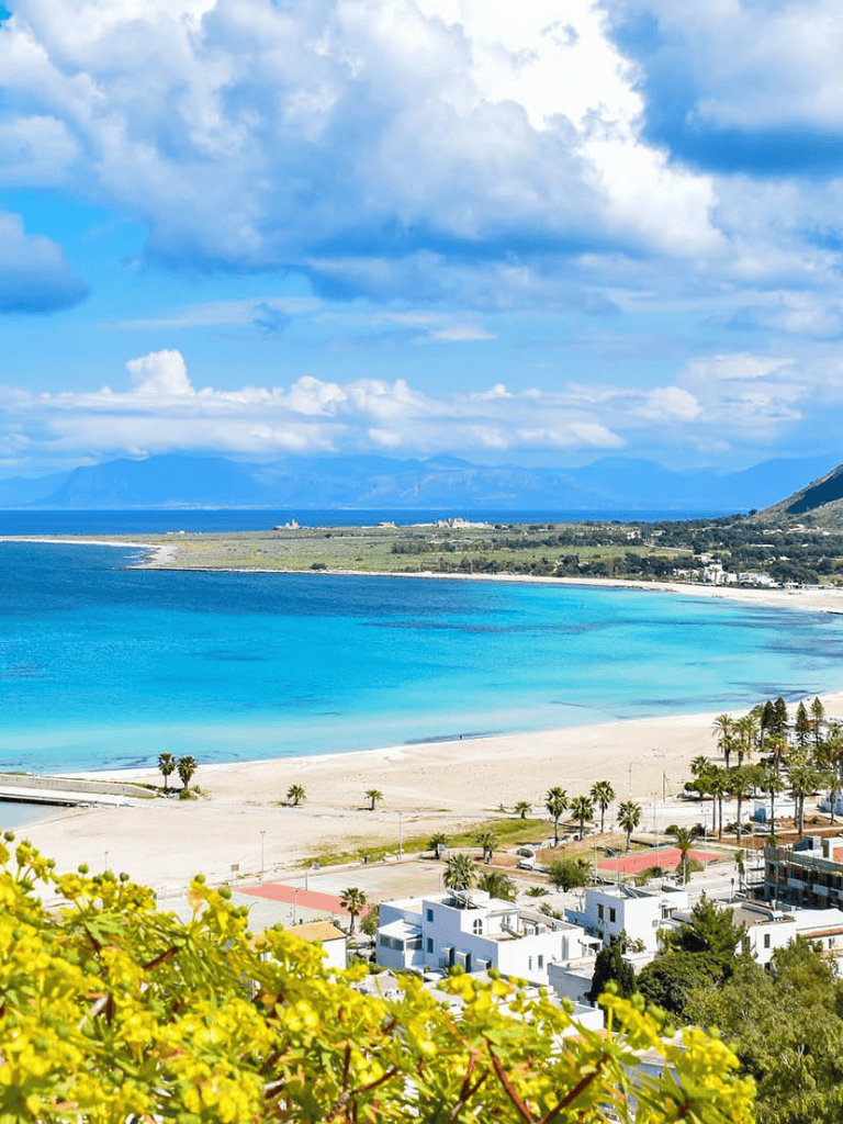 Stunning beach view of crystal-clear ocean, golden sand, and lush greenery with scenic backdrop.