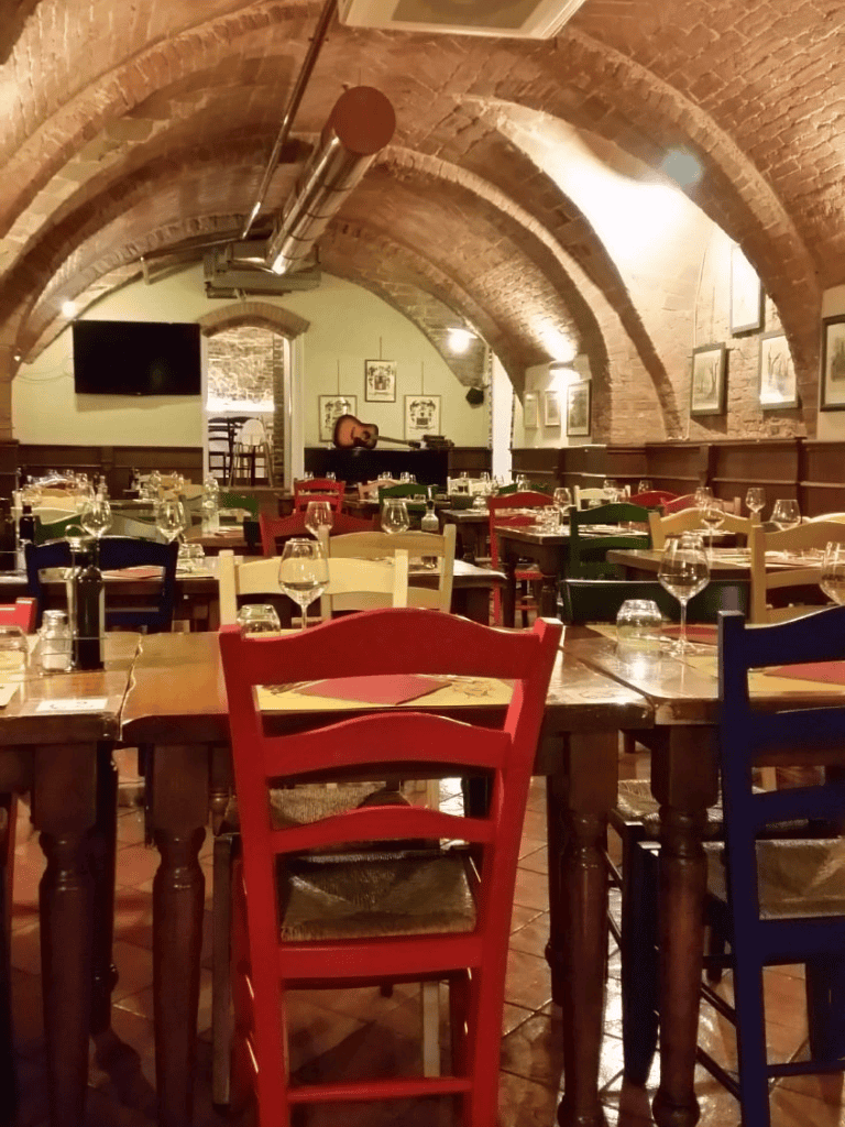 Cozy Italian restaurant with brick arches, colorful chairs, and elegant table settings.