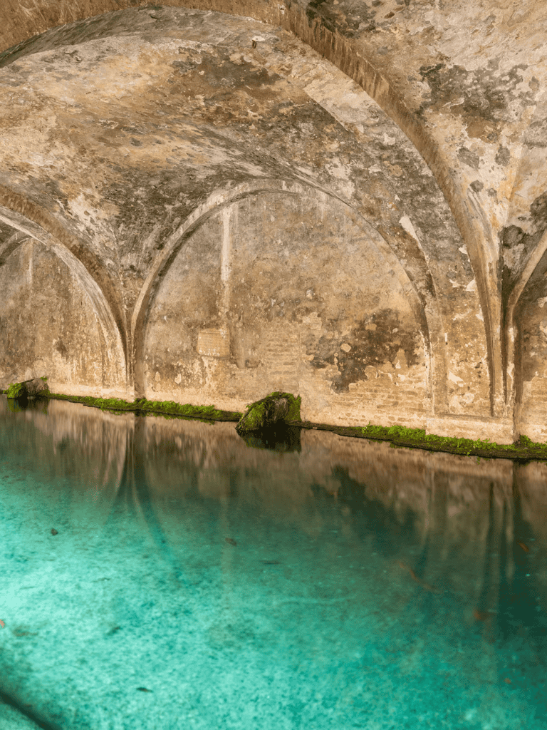 Ancient stone aqueduct with turquoise water and moss-covered stones, historical underground water tunnel.
