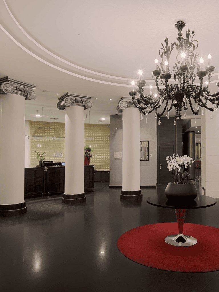 Chandelier hanging in elegant hotel lobby with white columns and floral decor.