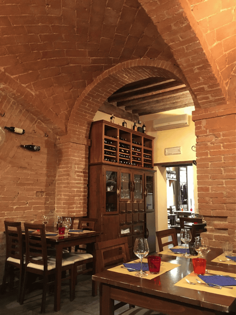 Cozy Italian restaurant interior with brick arches, wine display, and elegant table settings for dining.