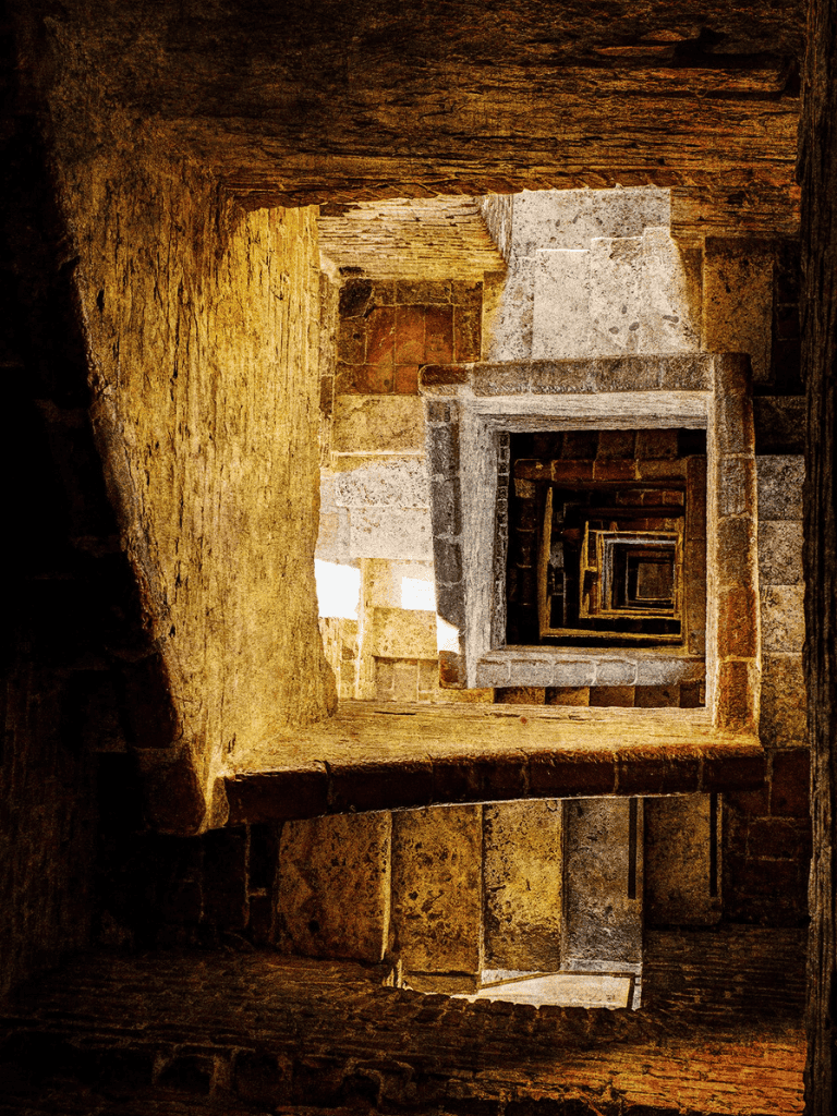 Ancient stone spiral staircase with historical architecture, indoor archaeological site, and rustic stone construction.