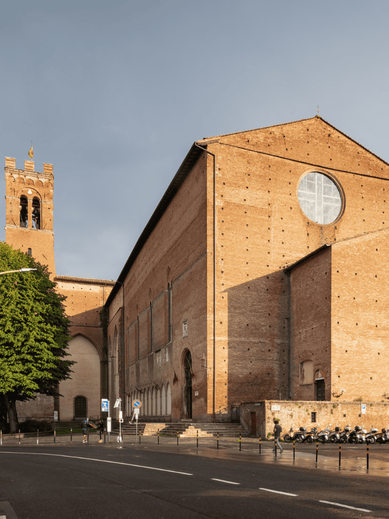 Ancient brick church building with a large circular window and a bell tower in the background.