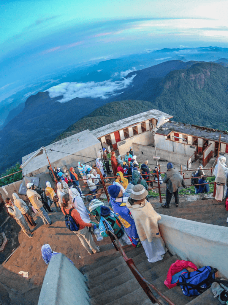 Elevated view of tourists at a mountain summit viewing platform overlooking lush green mountains and clouds, exploring adventure travel.