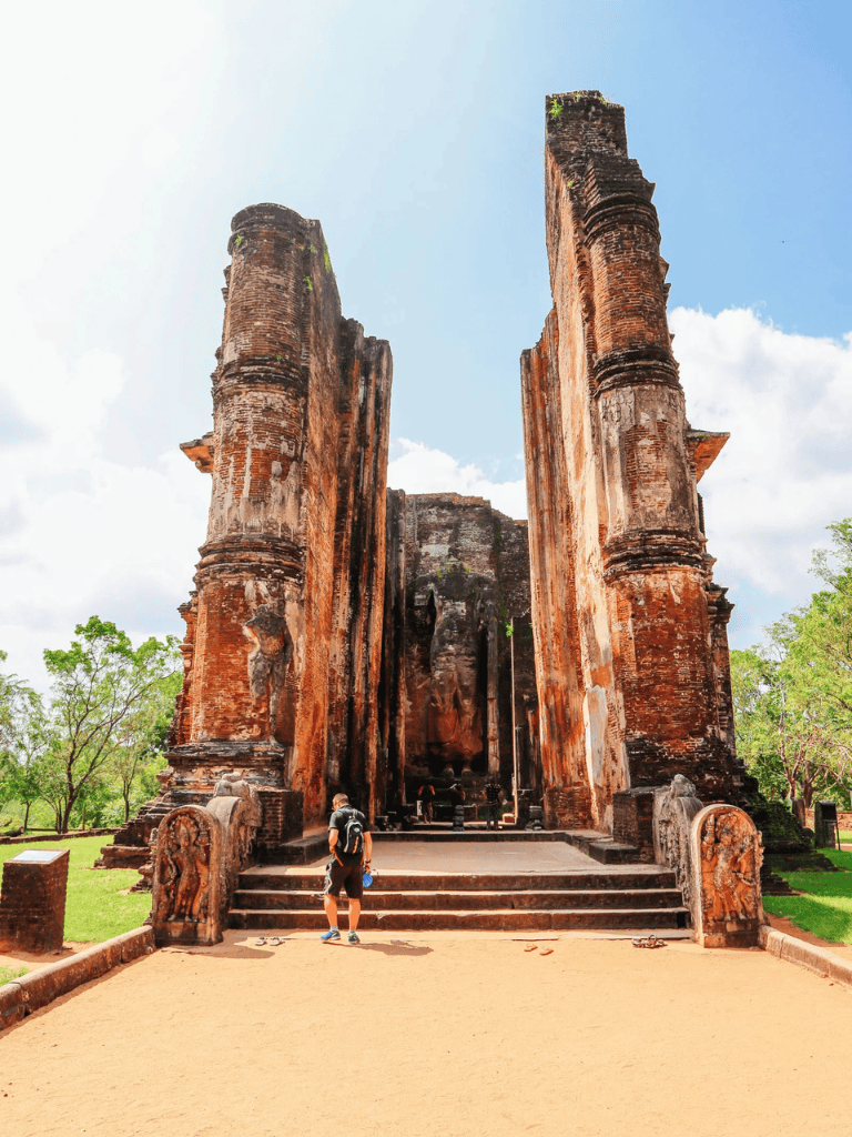 Ancient brick temple ruins with an open entrance, visitor exploring historic site, lush green surroundings, blue sky, cultural heritage.