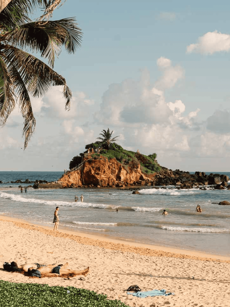 Tropical beach with palm trees and rocky island in the background, perfect for vacation and relaxation.