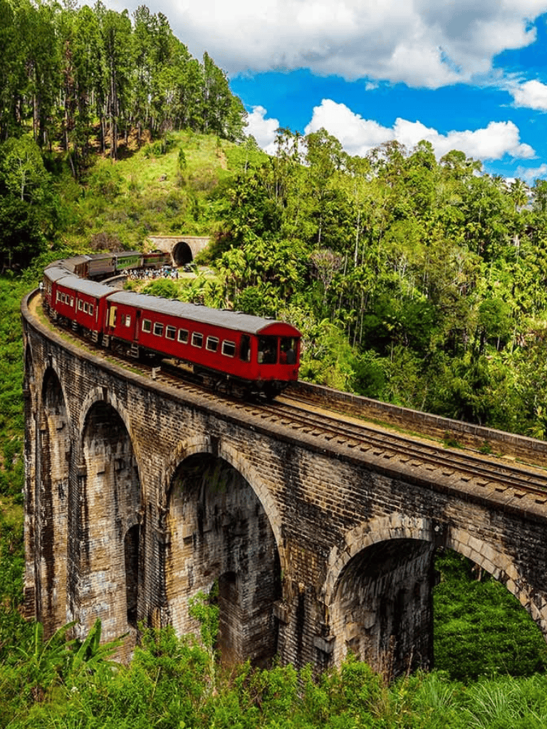 Vintage train traveling over historic brick bridge through lush green mountains.