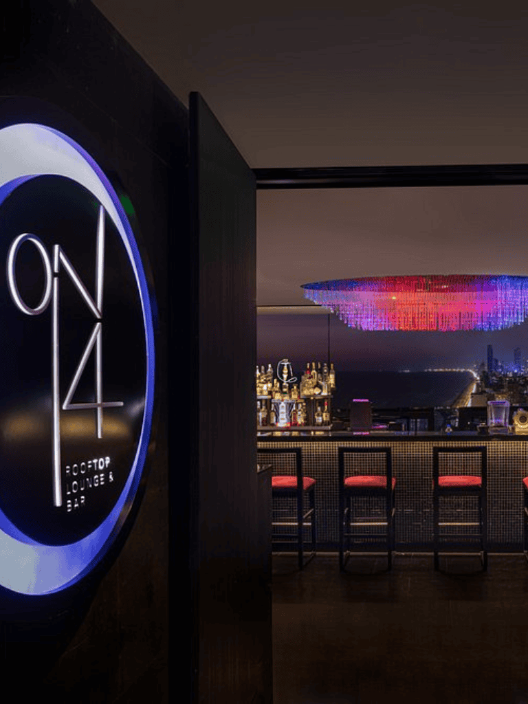 Elegant rooftop bar at night with city skyline view, modern decor, and colorful chandelier lighting for trendy nightlife experiences.