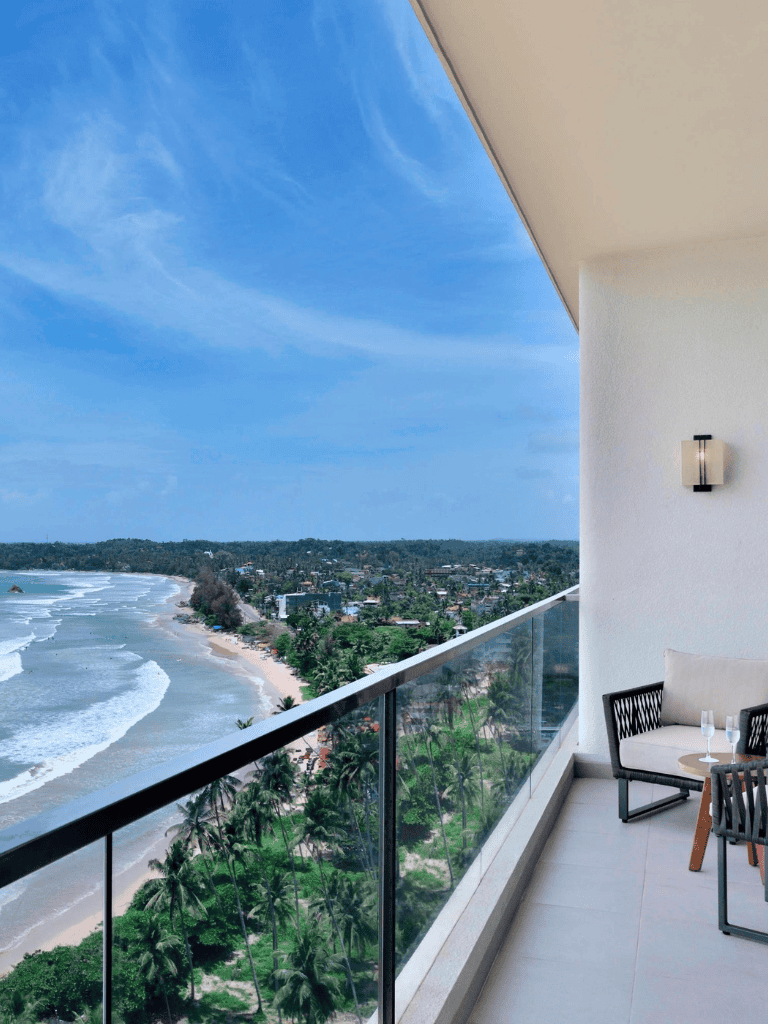 Stunning ocean view from balcony at QuestForDirections hotel with beach, palm trees, and clear blue sky.