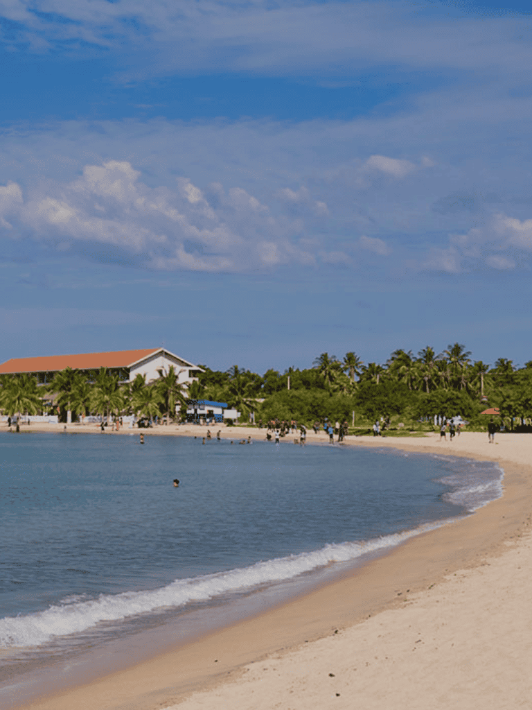 Beach with palm trees and a building, sunny sky, popular coastal destination for relaxation and vacation.