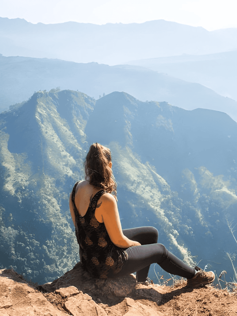 Serene woman sitting on mountain edge enjoying scenic view of lush green peaks and valleys.