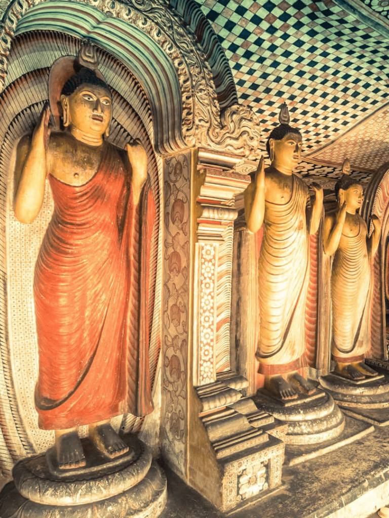 Ancient Buddhist statues inside a decorated temple with intricate ceiling patterns.