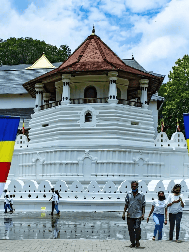 White historical monument at Wat Si Chum with visitors and colorful flags.