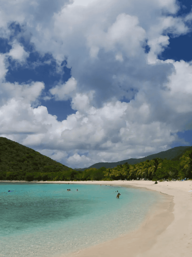 Stunning beach with turquoise waters and lush green mountains under a partly cloudy sky.
