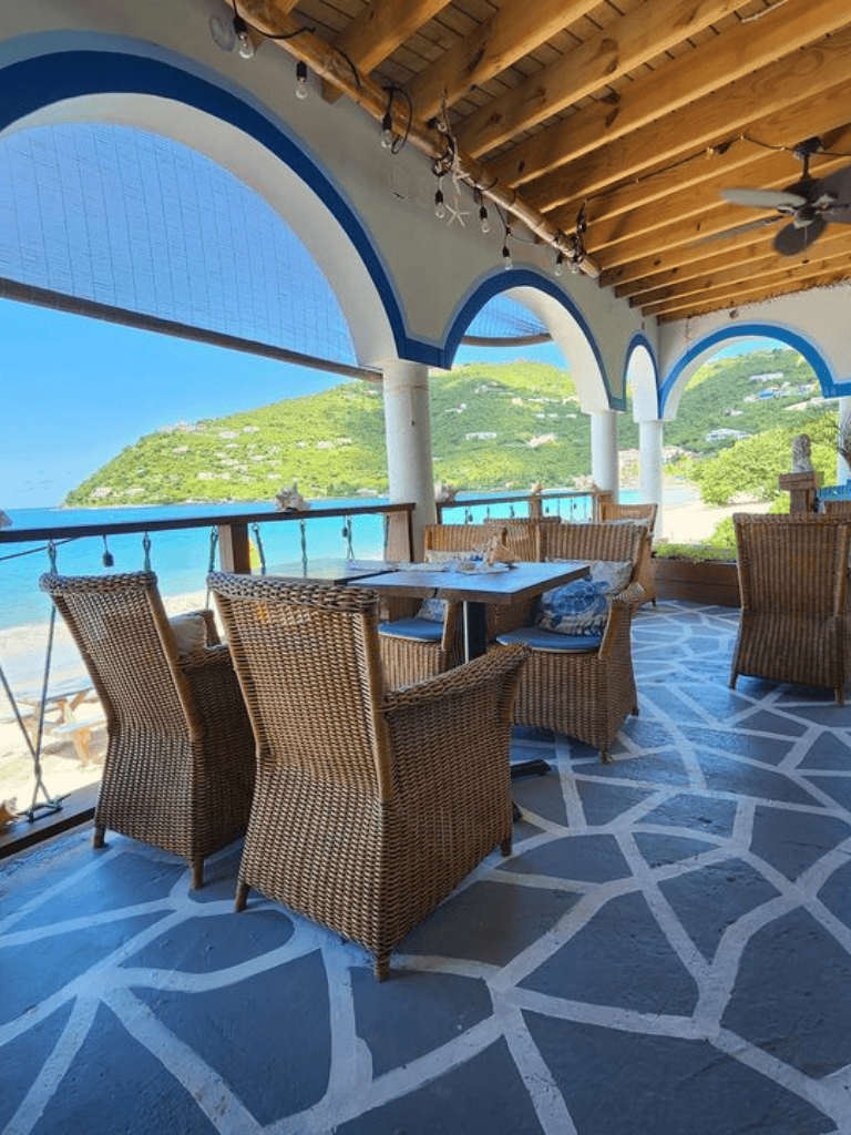 Beachside restaurant terrace overlooking ocean and lush hillside, ideal for relaxation and dining.