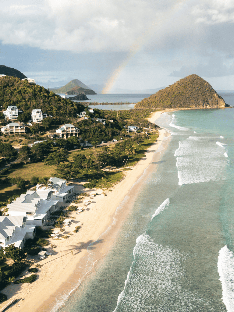 Stunning beach view with white villas, lush greenery, and a rainbow over the ocean in a tropical destination.