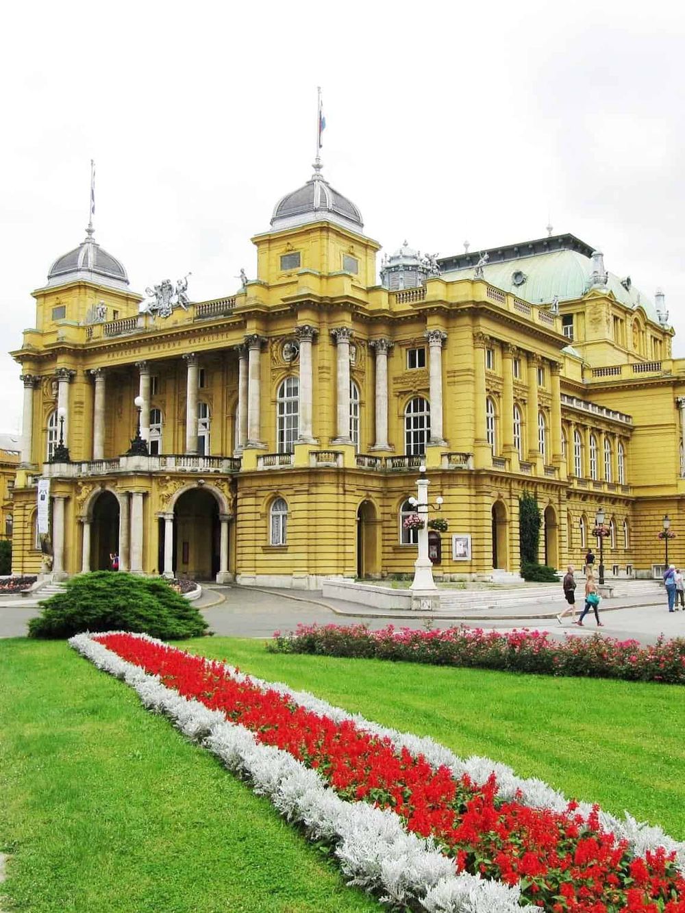 Elegant historic yellow palace with lush flower garden, central stairs, and decorative architecture, perfect for travel and tourism.