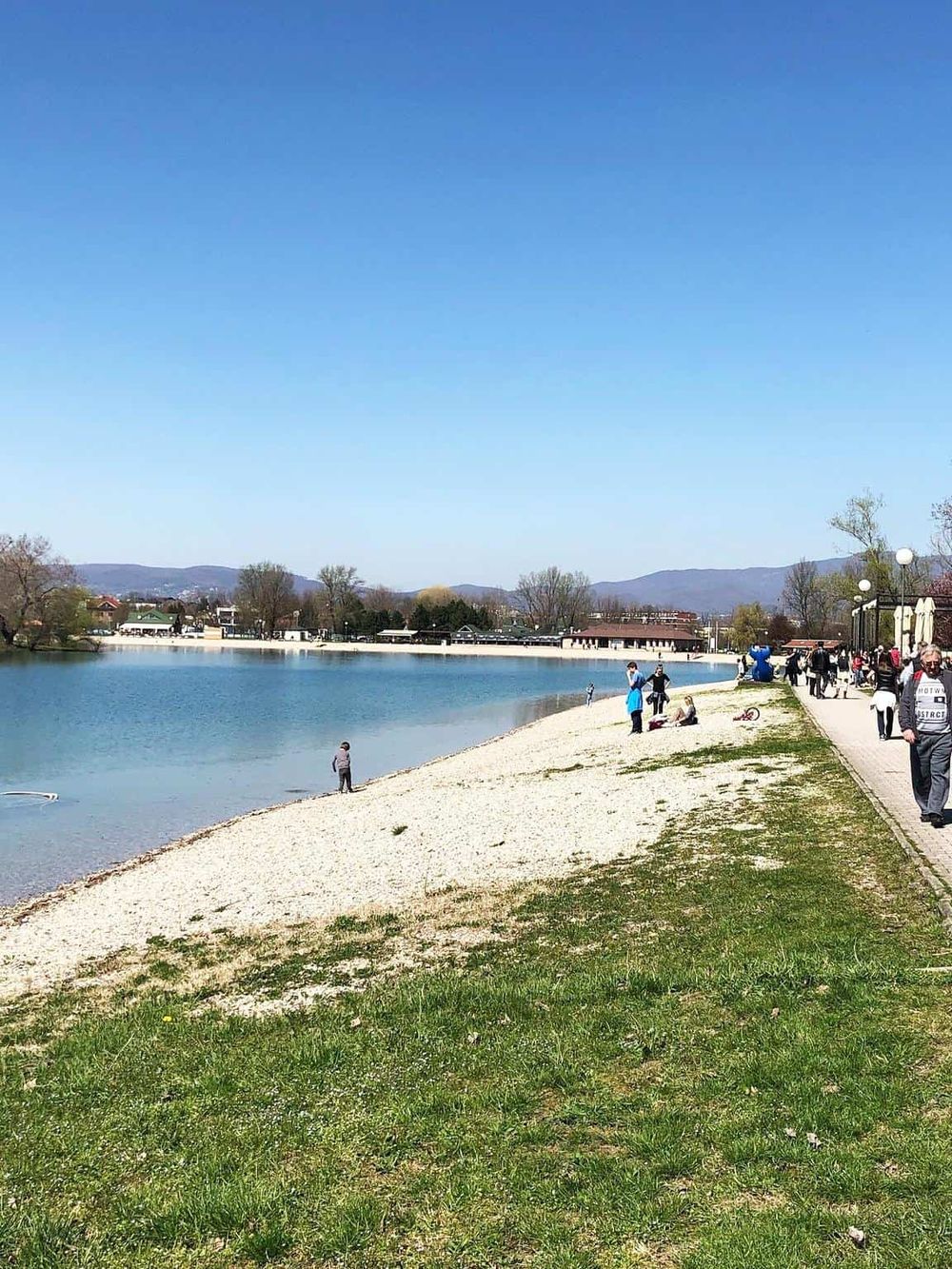 Serene lakeside view with a sandy beach and people enjoying outdoor activities in a peaceful town setting.