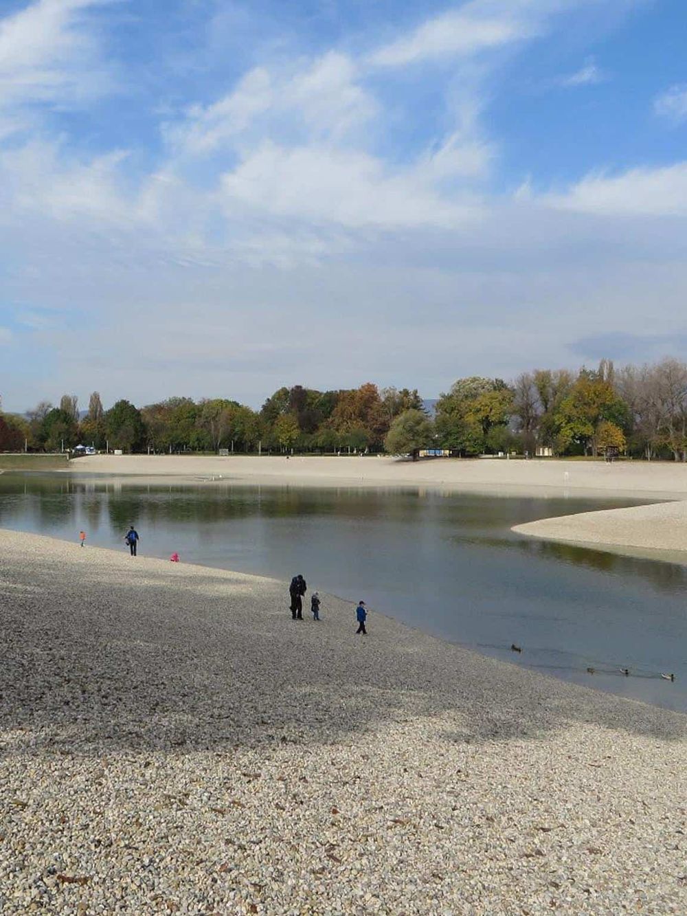 Serene lakeside park during daytime with people walking and enjoying nature, perfect for outdoor activities and relaxation.