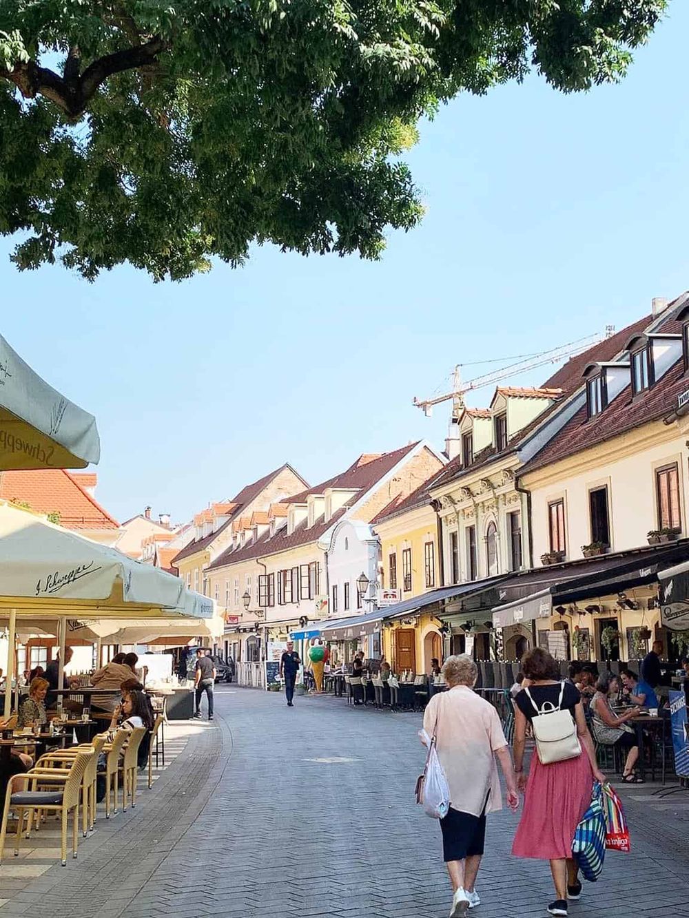 Charming outdoor cafe on a European street with colorful buildings and pedestrians enjoying the sunny day.