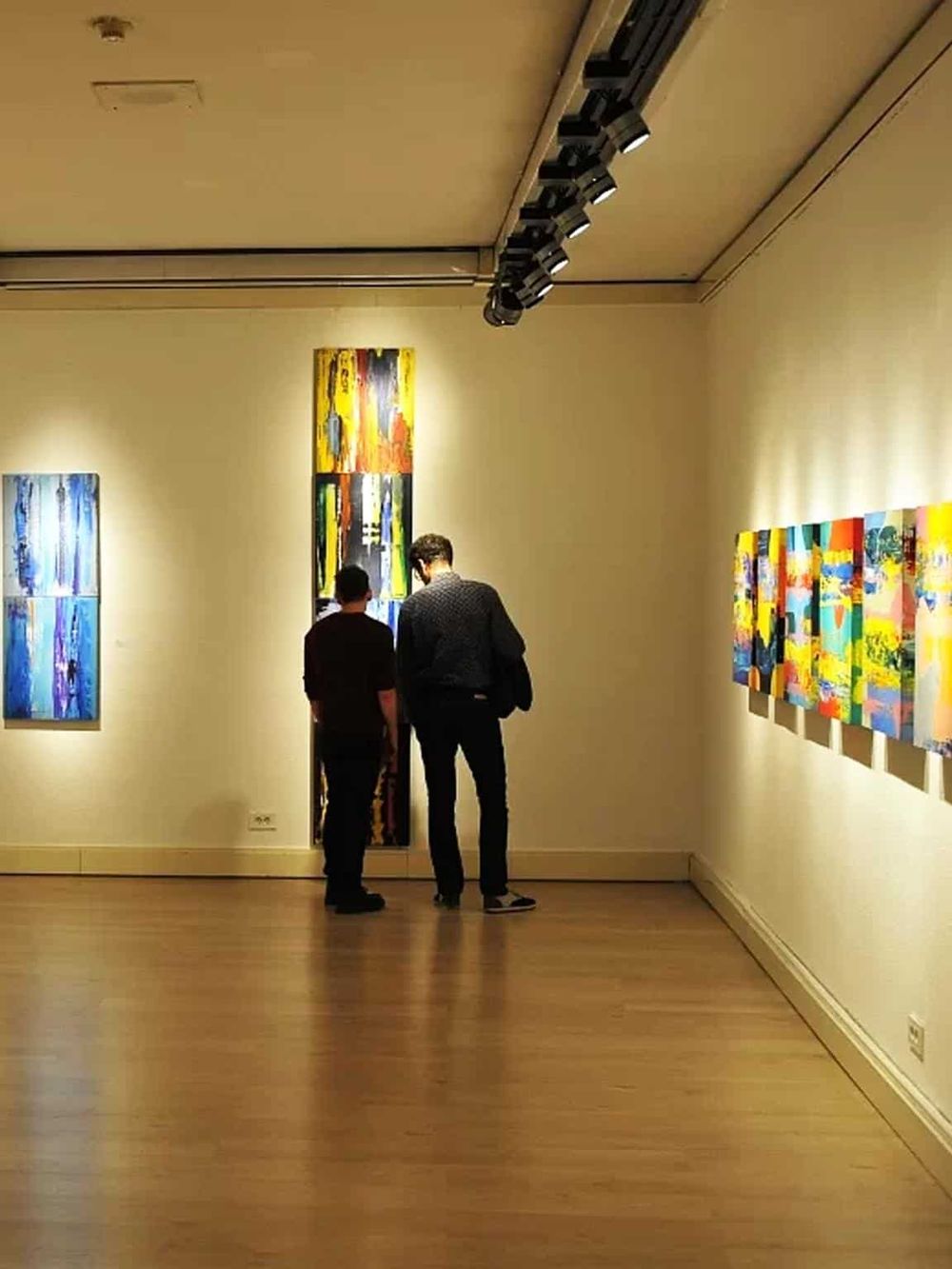 Colorful abstract art displayed in gallery with visitors viewing artwork.