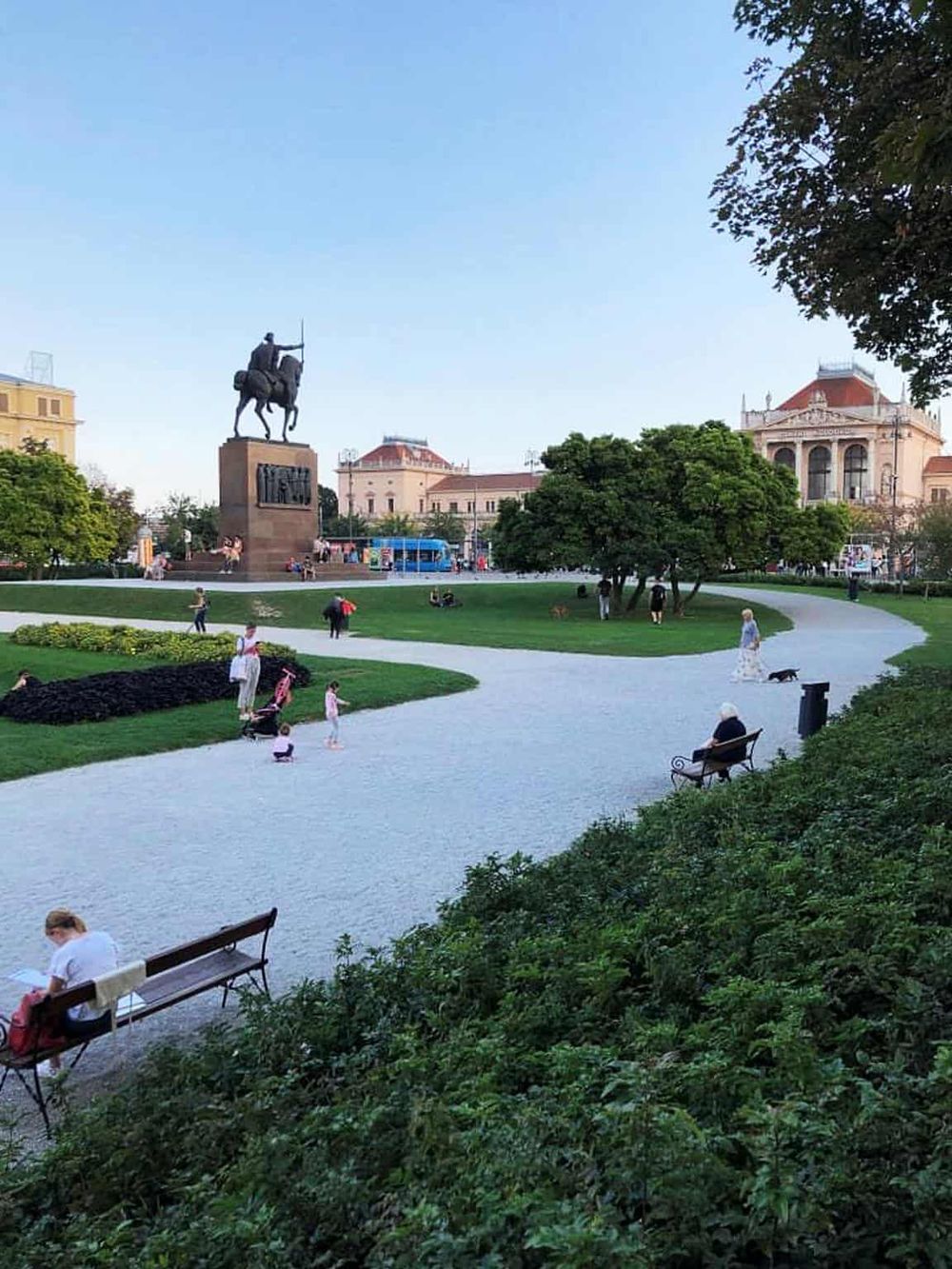 Historic city park with a large equestrian statue, lush greenery, and visitors enjoying the outdoor space.