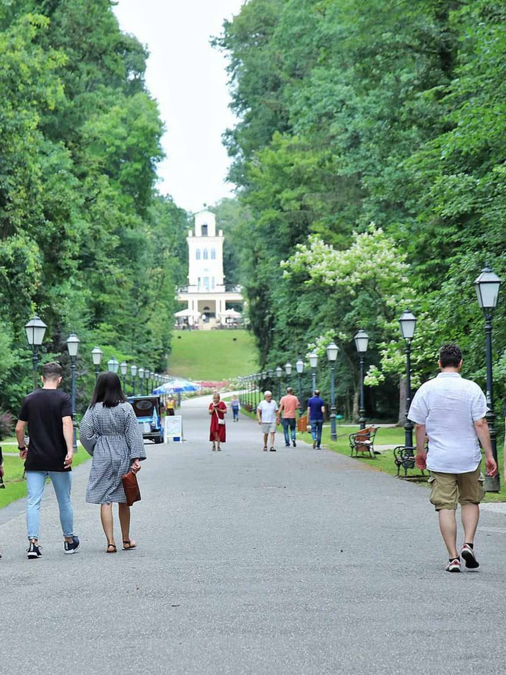 Lush park pathway leading to Quest for Directions landmark, surrounded by green trees and visitors.