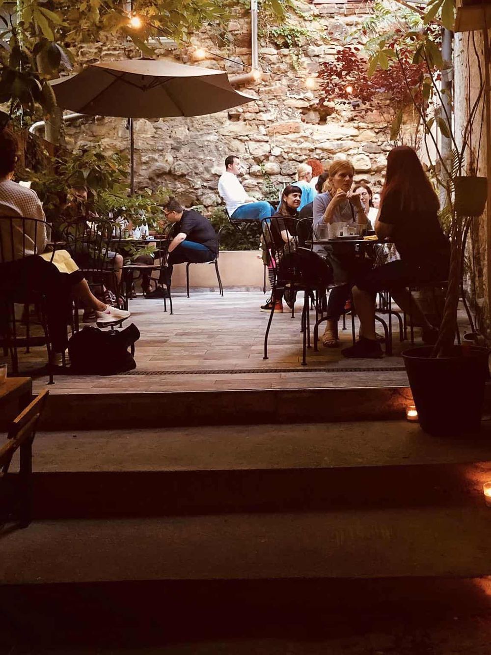 Cozy outdoor dining area at QuestForDirections, featuring string lights, greenery, and rustic stone walls.