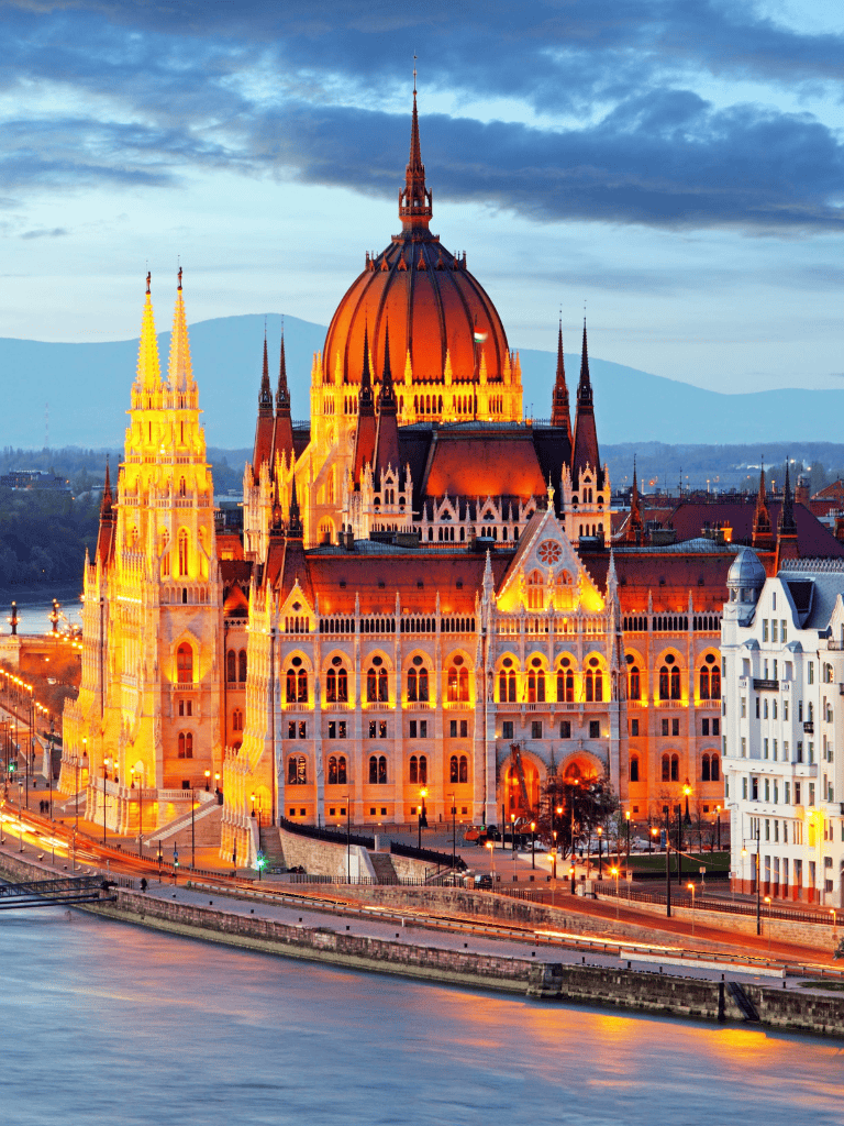 Majestic Hungarian Parliament Building at dusk in Budapest, illuminated by warm lights along the Danube River.