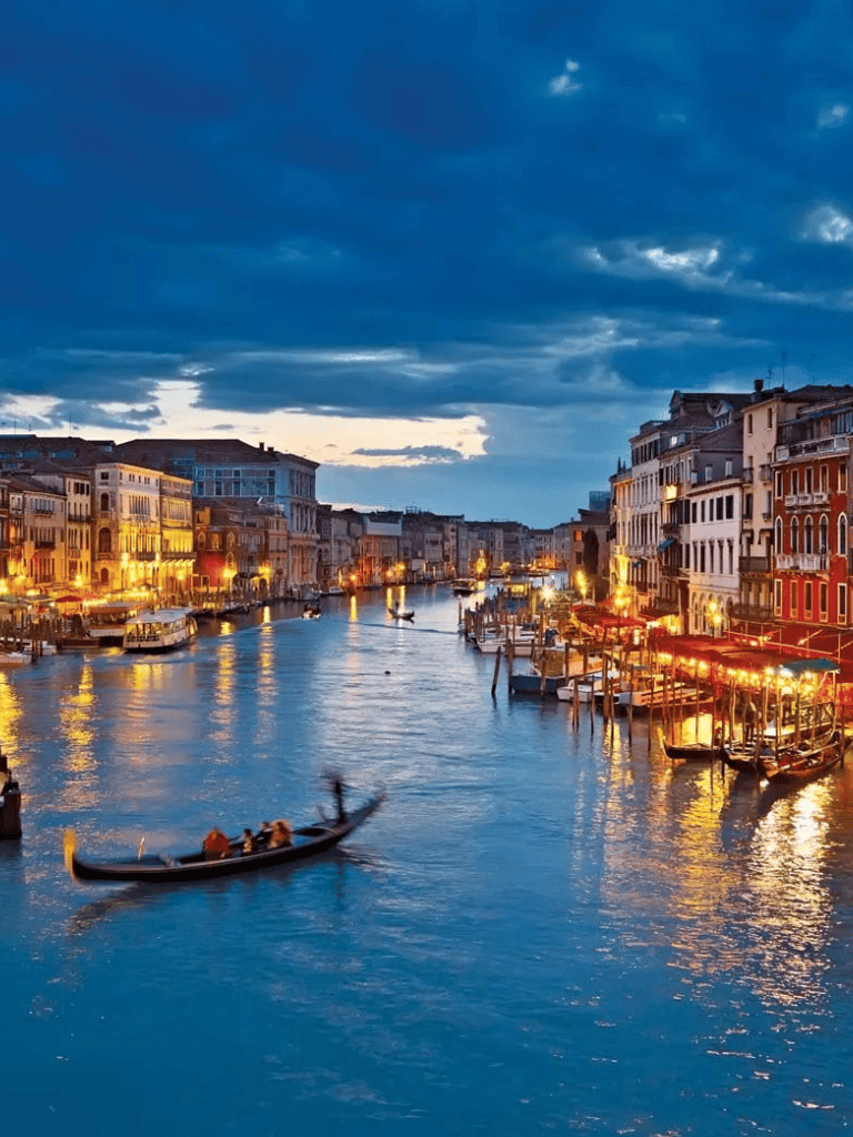Vibrant evening view of Venice canals with illuminated historic buildings and gondolas.