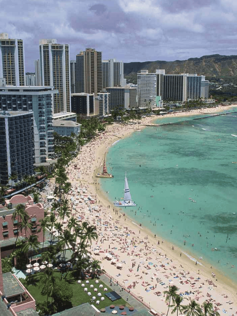 Luxurious Waikiki Beach with high-rise hotels and sailboats, Honolulu skyline, panoramic ocean views, Hawaii travel destination.