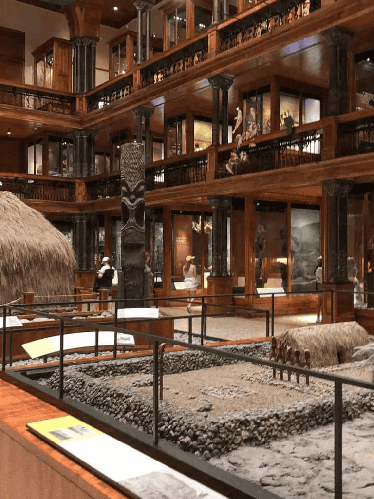 Ancient Polynesian artifacts and wooden architecture in a cultural museum exhibit.