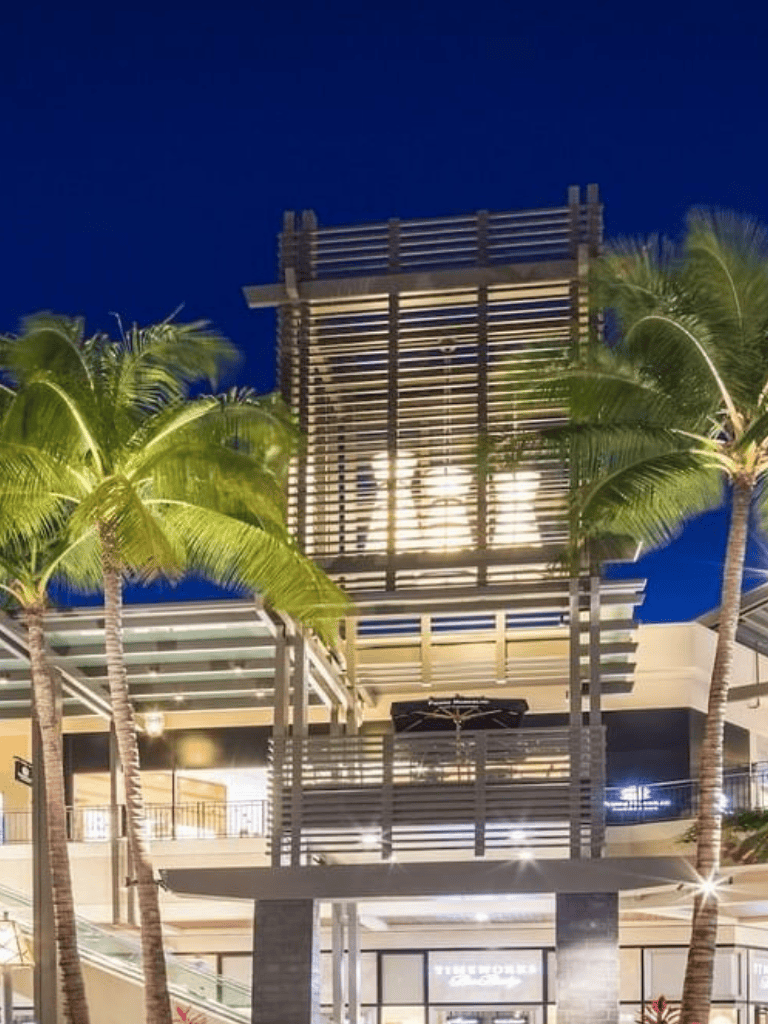 Stylish modern shopping mall with outdoor seating and palm trees at night, illuminated by strategic lighting.