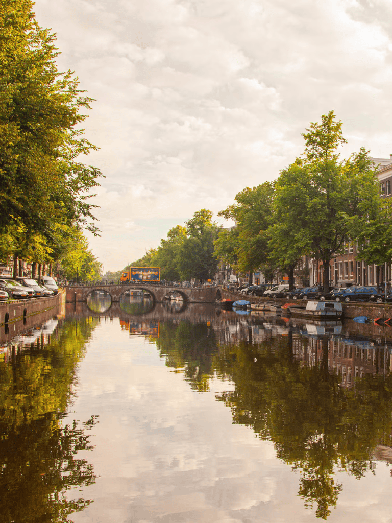 Serene canal scene with historic bridges and lush trees, perfect for sightseeing in Amsterdam.